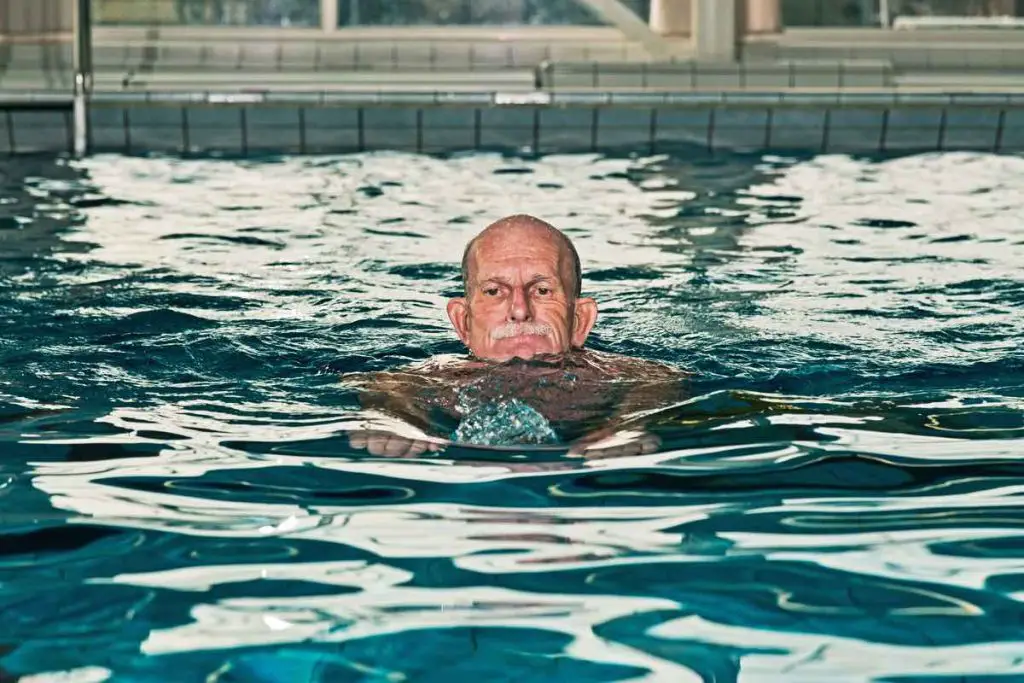 Healthy senior man with beard in indoor swimming pool.