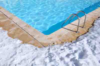 blue water of a swimming pool with outdoor terrace covered in snow
