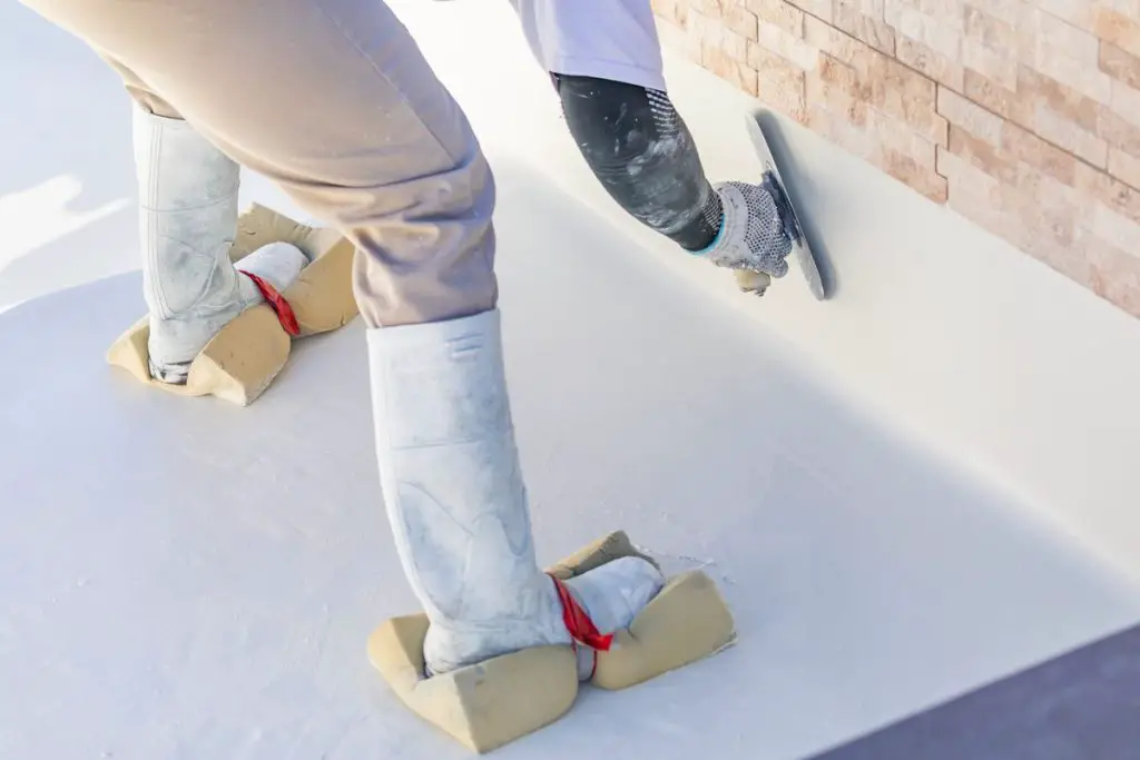 Worker Wearing Sponges On Shoes Smoothing Wet Pool Plaster With Trowel.