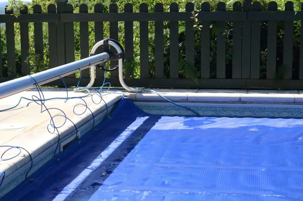 Swimming pool cover off its roller and covering the pool