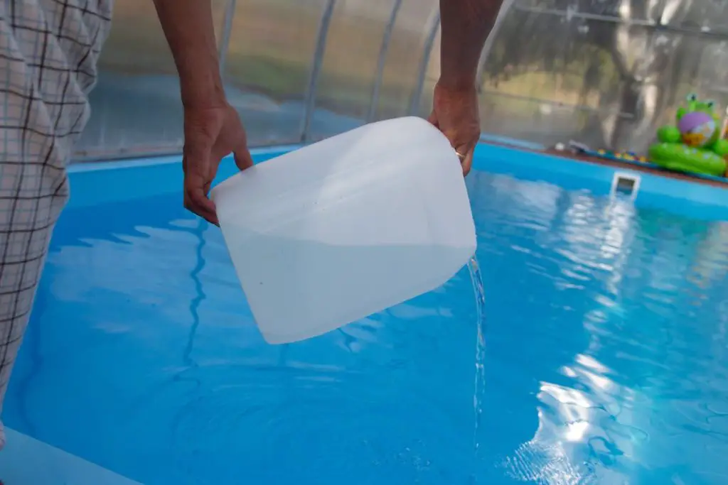 men's hands pour light liquid from a plastic tank into a pool, into water. chemical water purification, alkali balance, unsanitary conditions.disinfection and preparation for swimming. care for the pool