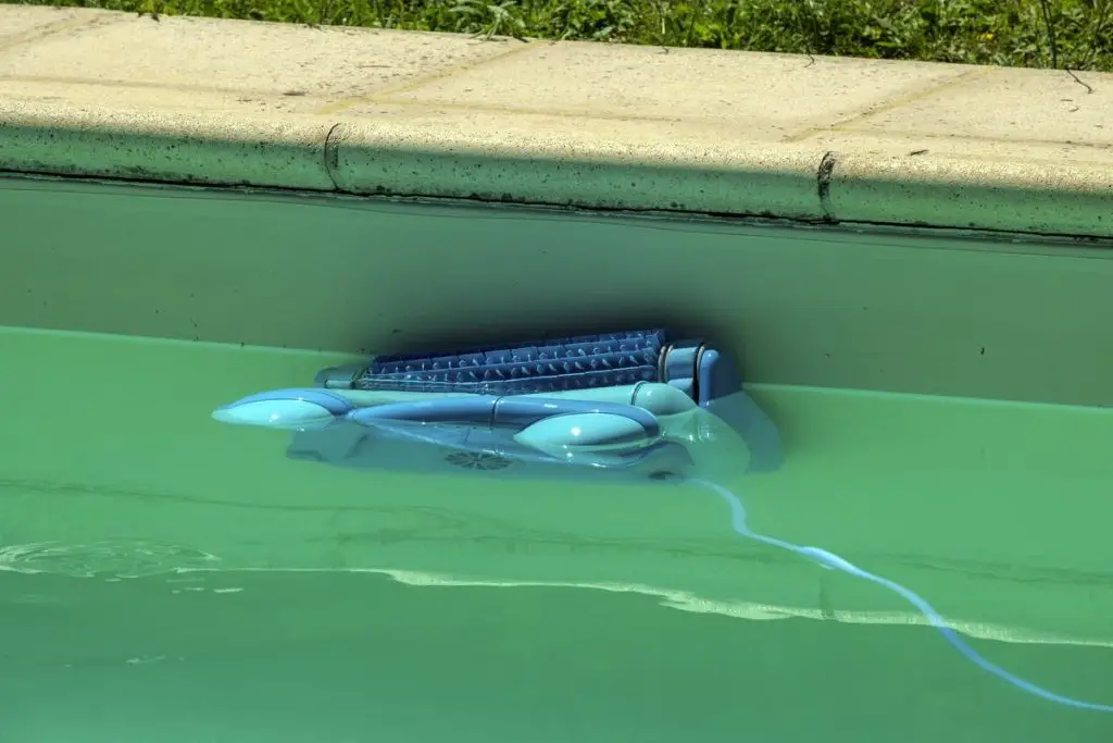 An automatic robot pool cleaner climbs the side of a cloudy swimming pool removing debris and algae