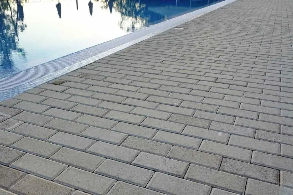 The Edge Of Swimming Pool With Calm Blue Crystal Clear Water And Concrete Paving Floor In Perspective View. Summer Evening Time.