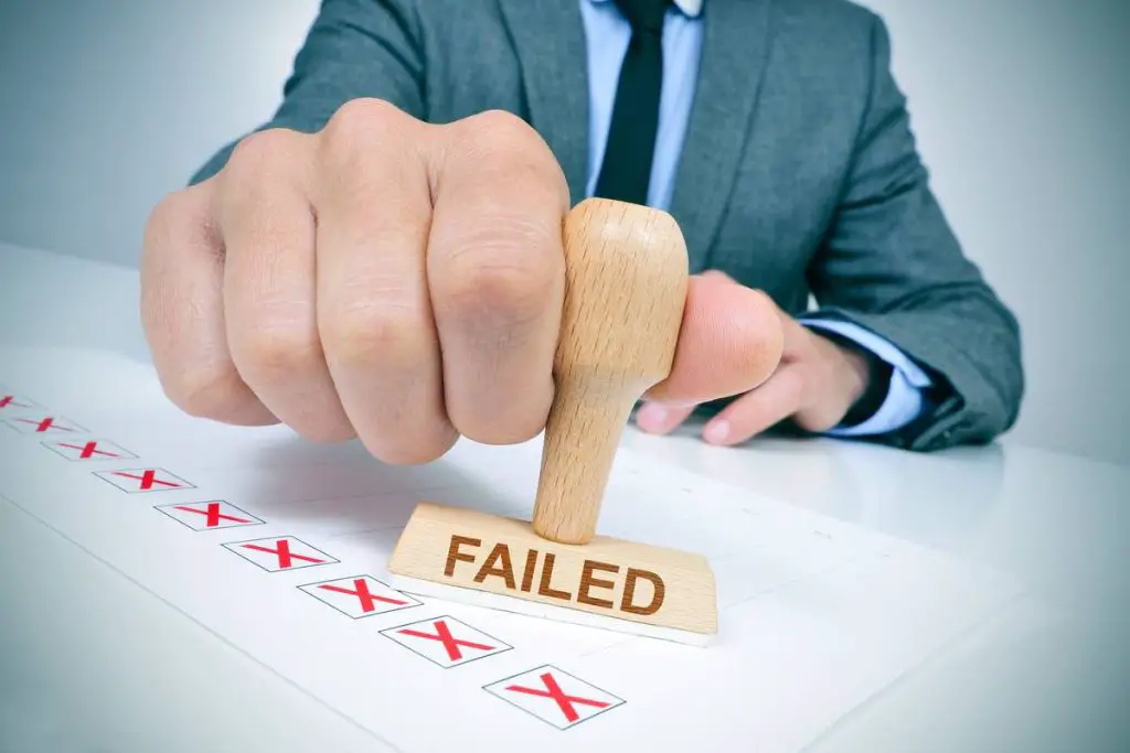 a young caucasian man at his office desk with a rubber stamp with the word failed