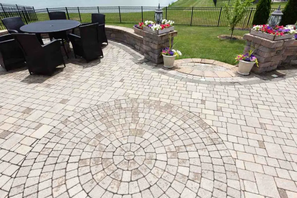 Ornamental brick paved outdoor patio with a circular design in the bricks with dining furniture and colorful flowers in flowerpots flanking steps and an entrance, view from above after rain